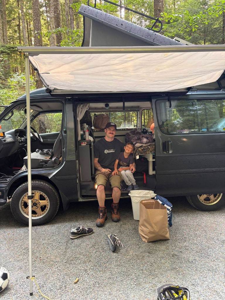 Kody and his son Isaiah sitting in the doorway of their imported HiAce camper