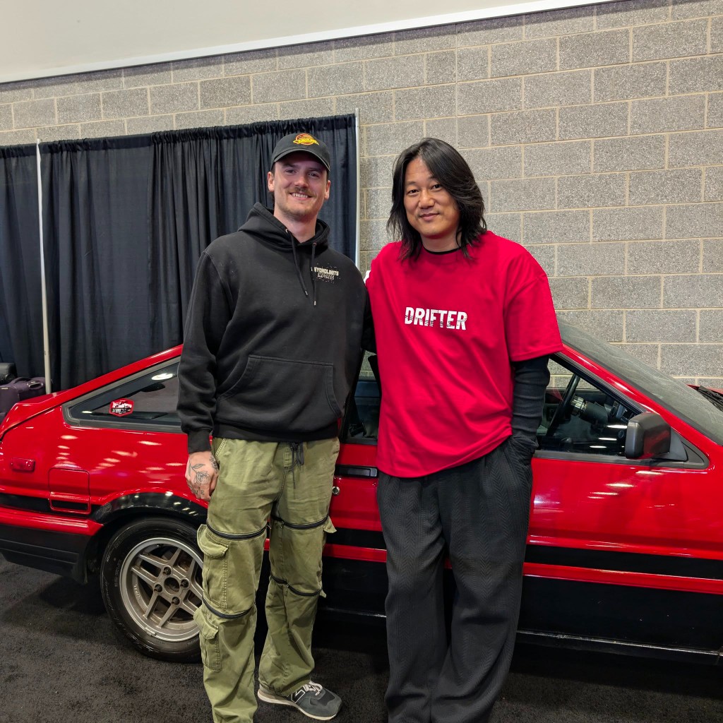 Kody with Sung Kang in front of a red Toyota AE86 at a JDM car show